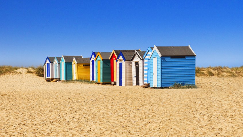 Multicoloured beach huts on a sandy beach against a bright blue sky